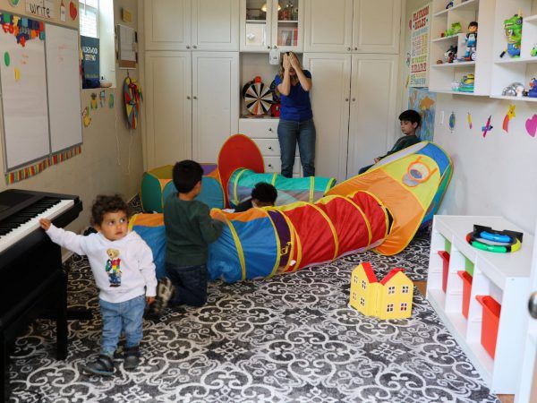 two young children playing in a playroom together with the piano, while another kid is watching