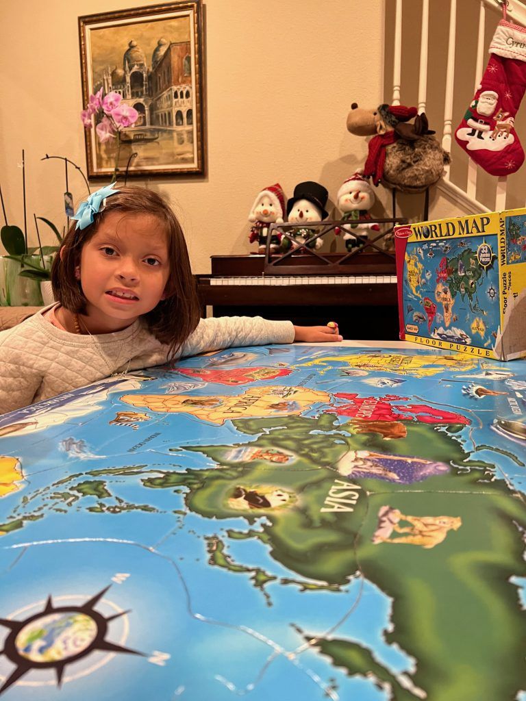 The girl in a white sweater playing with a puzzle-puzzle on the desk.