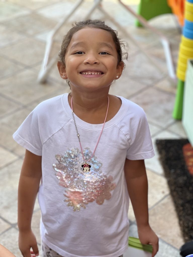 Sweet little girl outdoors with curly hair and white shirt.