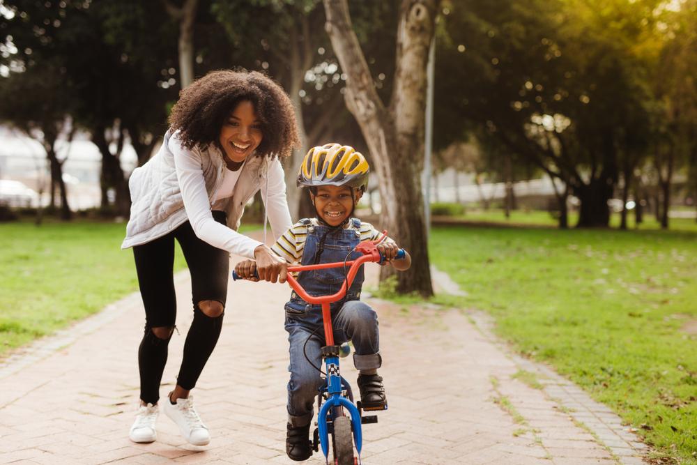 Happy cute boy learn to ride a bike with his mother. Mother teaching son to ride bicycle at park.
