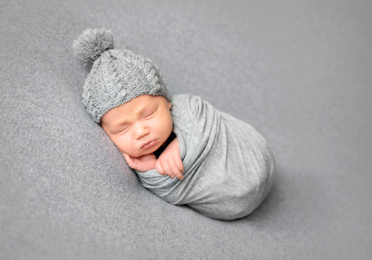 A swaddled newborn baby sleeping in a bonnet.