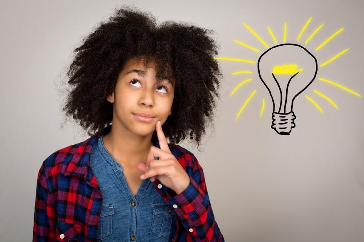 A young teenage girl with wacky afro hair looking up, thinking, and solving problems isolated against a grey background.