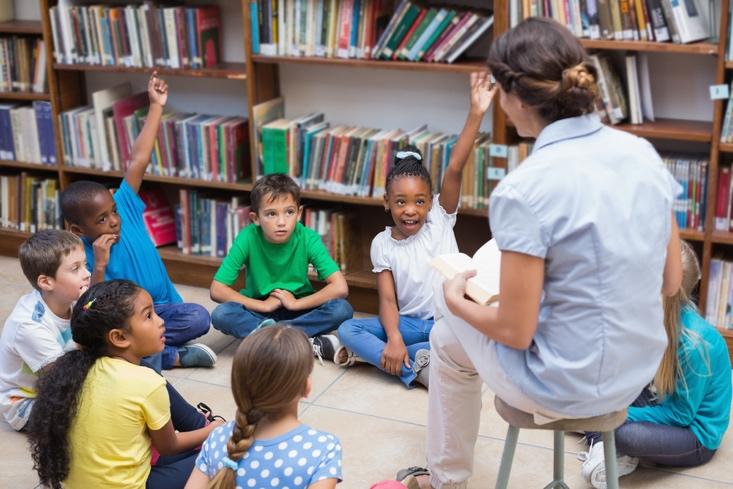 cute pupils and teacher having class in the library at the elementary school