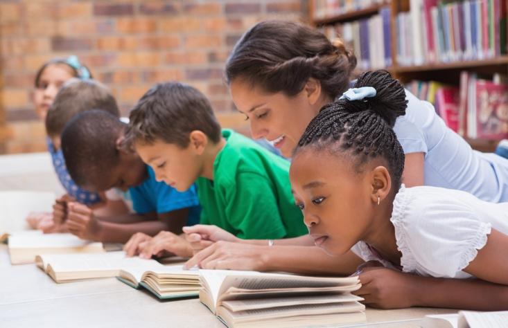 Cute pupils and teacher lying on the floor in the library at the elementary school