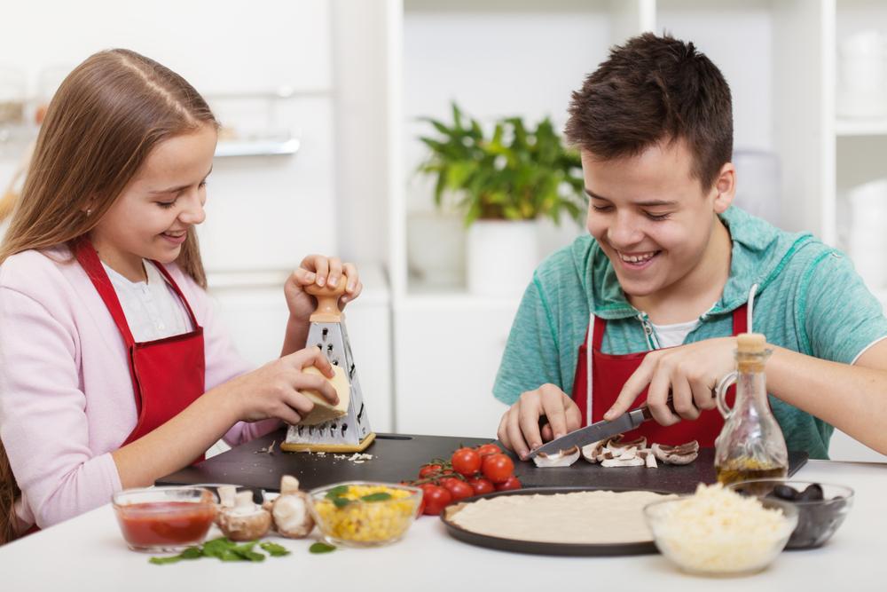 Happy teenagers having fun in the kitchen preparing a pizza and chatting with broad smiles on their faces