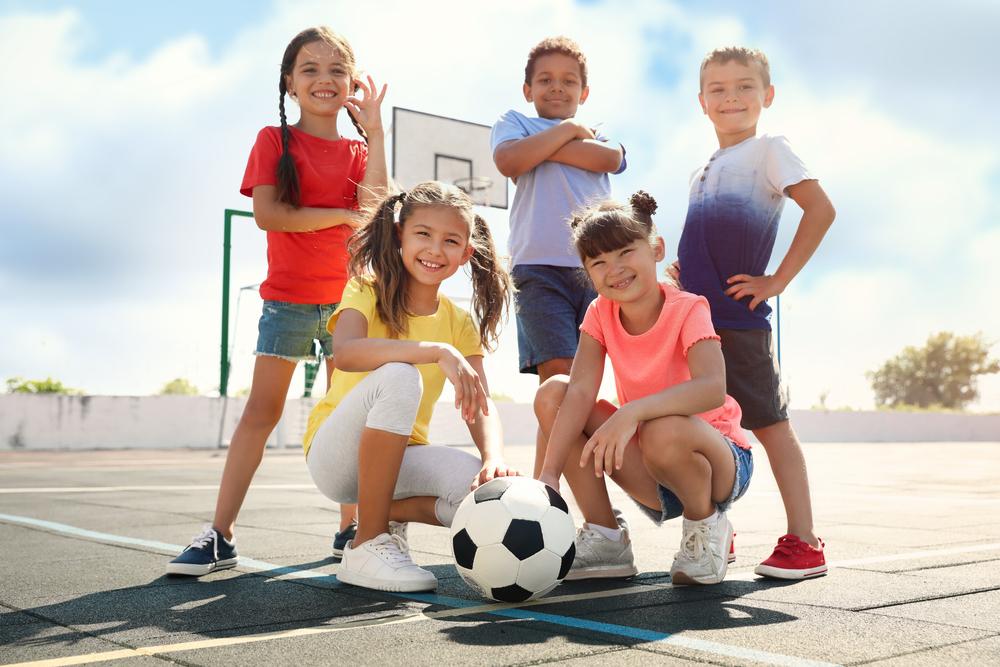 cute children with soccer ball at sports court on sunny day. Summer camp