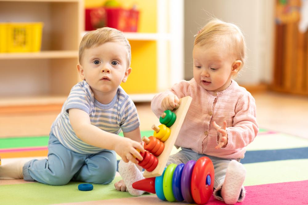 funny baby boy and toddler girl playing on the floor in the game room in the nursery