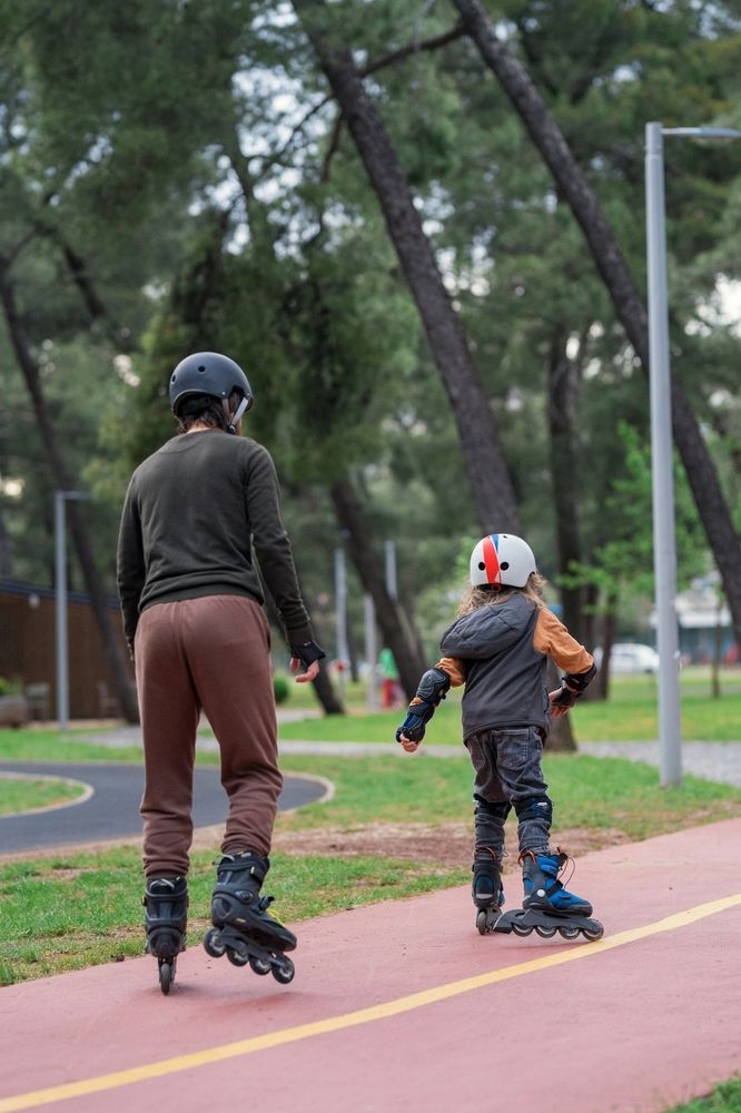 Father and son in protective gear go rollerblading deep into the park