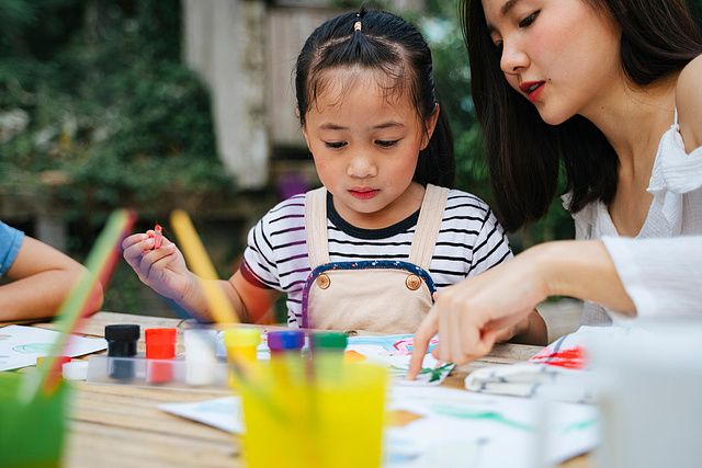 Asian big sister helping little sister painting water colour on paper outdoors.