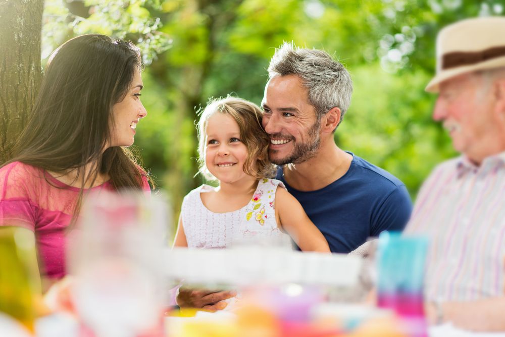 Three generations family gathered to lunch in the garden in summer, they having fun sitting around a picnic table.