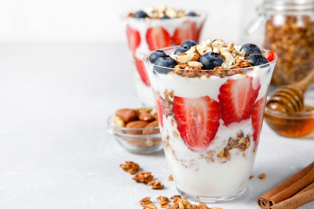 Granola Parfait with greek yogurt, oat granola, fresh berries, honey and mint leaves in tall glass jar. Healthy breakfast concept. Organic oat, almond and sunflower seeds.
