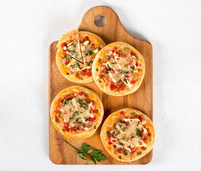 Open small pies, mini pizzas with sausage, pickles, tomatoes, mozzarella, parsley on a wooden board on a light background top view