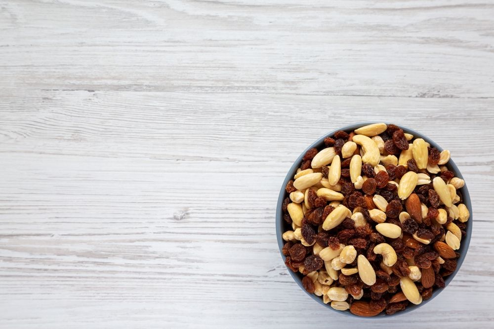 Raw Trail Mix with Nuts and Fruits in a Bowl on a white wooden background, top view. Flat lay, overhead, from above. 