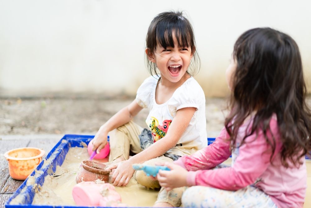 Adorable 4 years old asian little girl is playing the sand mud with her unidentified friend with fully happiness moment, concept of outdoor freeplay for kid development and social skill