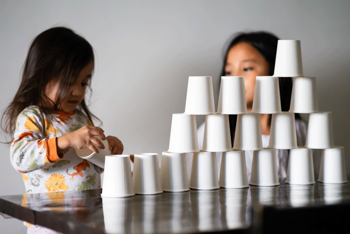 Kids Playing with white paper cups building a cup tower on the table. Sisters, siblings playing together.