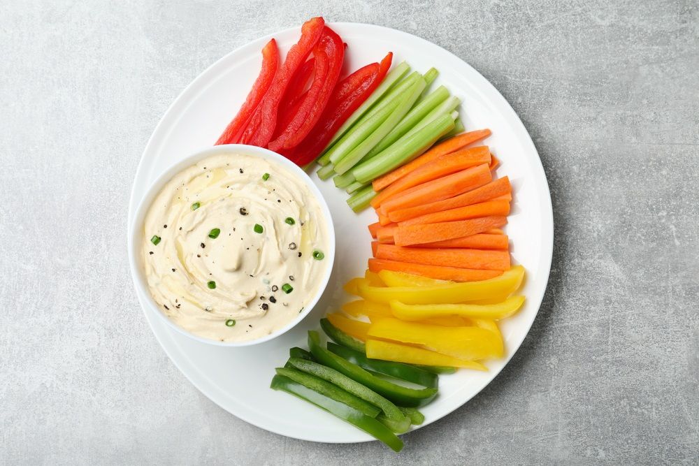 Fresh raw vegetable sticks and sauce on grey table.