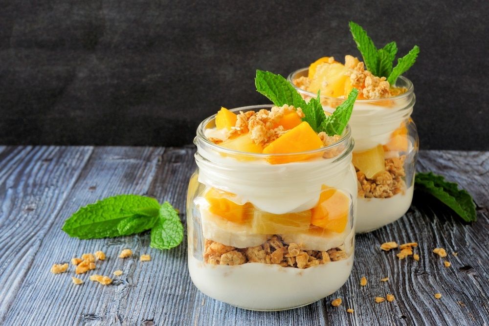 Tropical mango and pineapple parfaits in mason jars, scene on dark rustic background