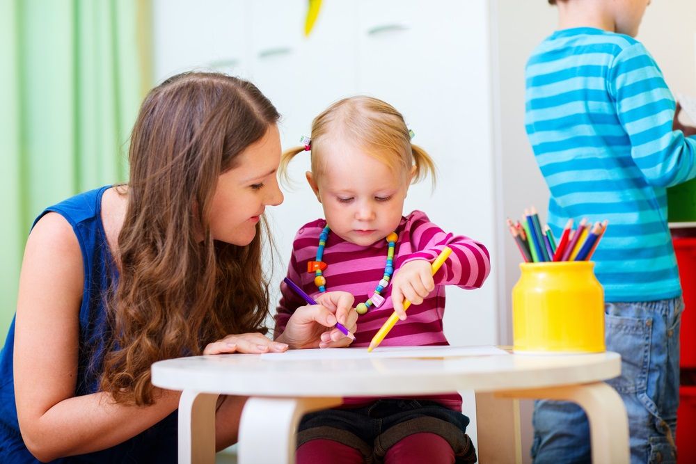 Group of workers with babies in nursery or kindergarten