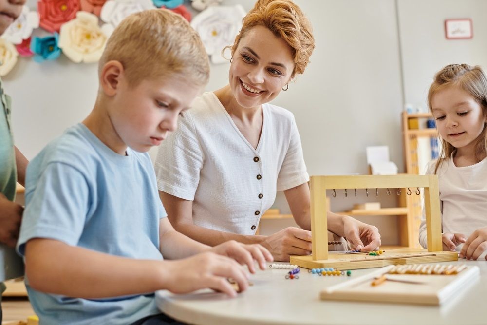 montessori materials, happy female teacher observing concentrated boy near children during class