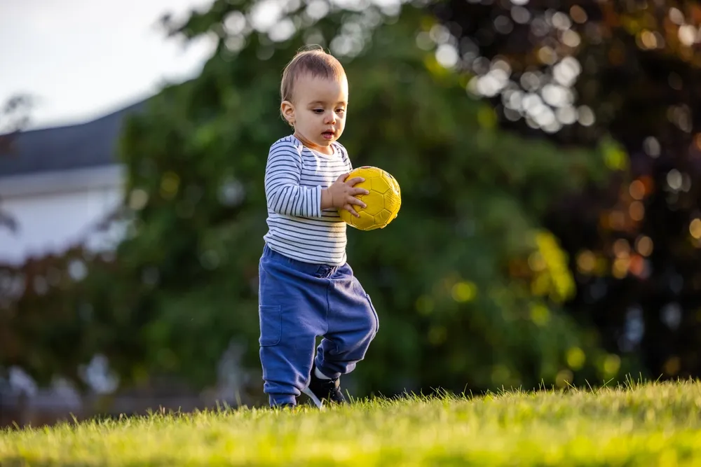 Toddler rolling a soft ball toward a goal during supervised outdoor play 